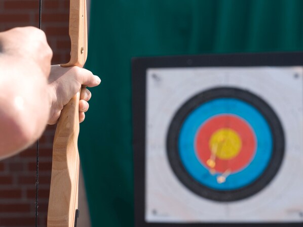 A hand holding a bow, aiming at a target with concentric circles.