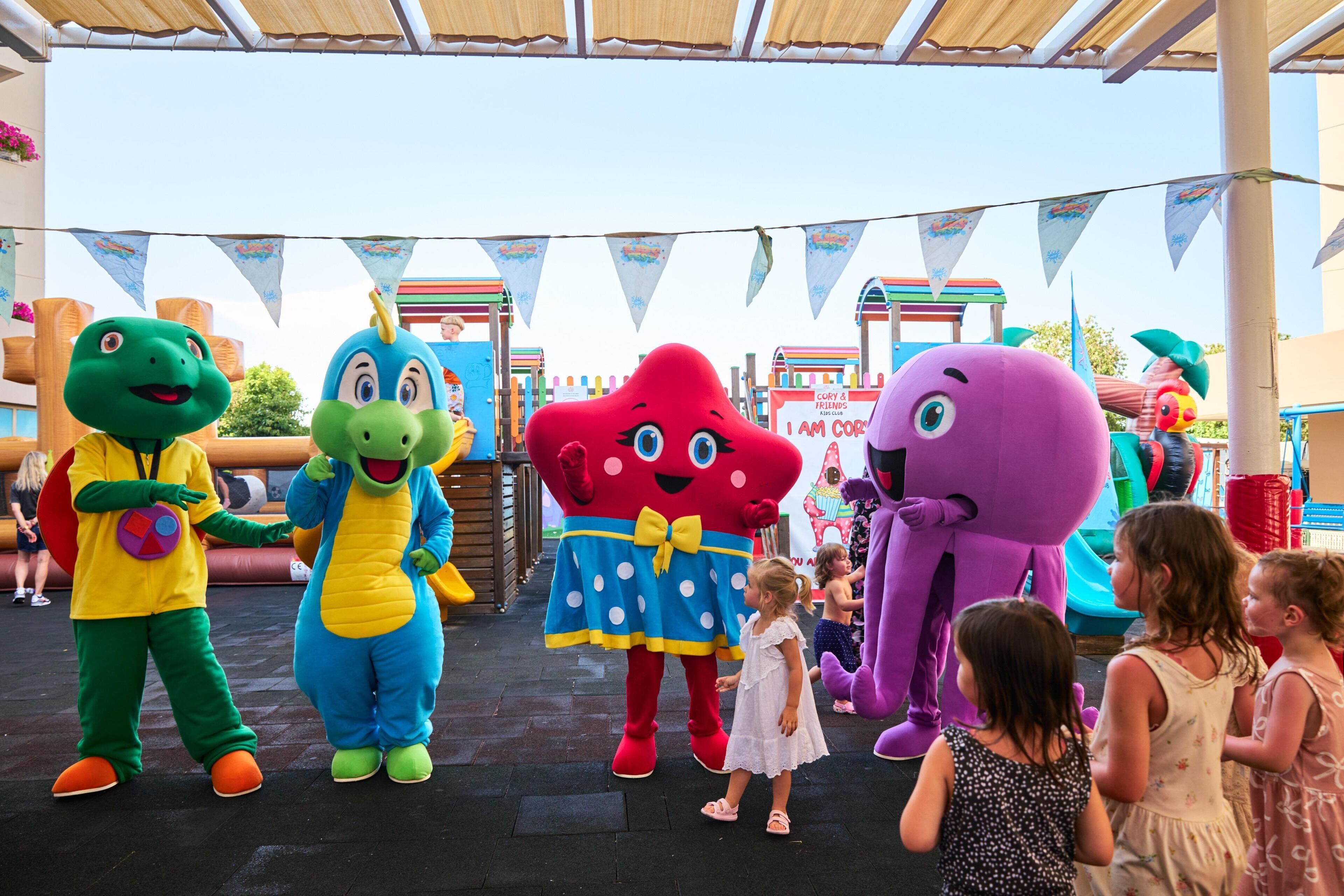 Un grupo de personajes mascota coloridos interactuando con niños en un evento temático.