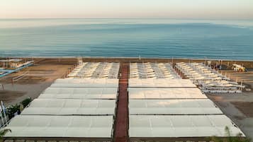 Un hotel frente al mar con múltiples toldos blancos y filas de sillas de playa, con vista al océano.