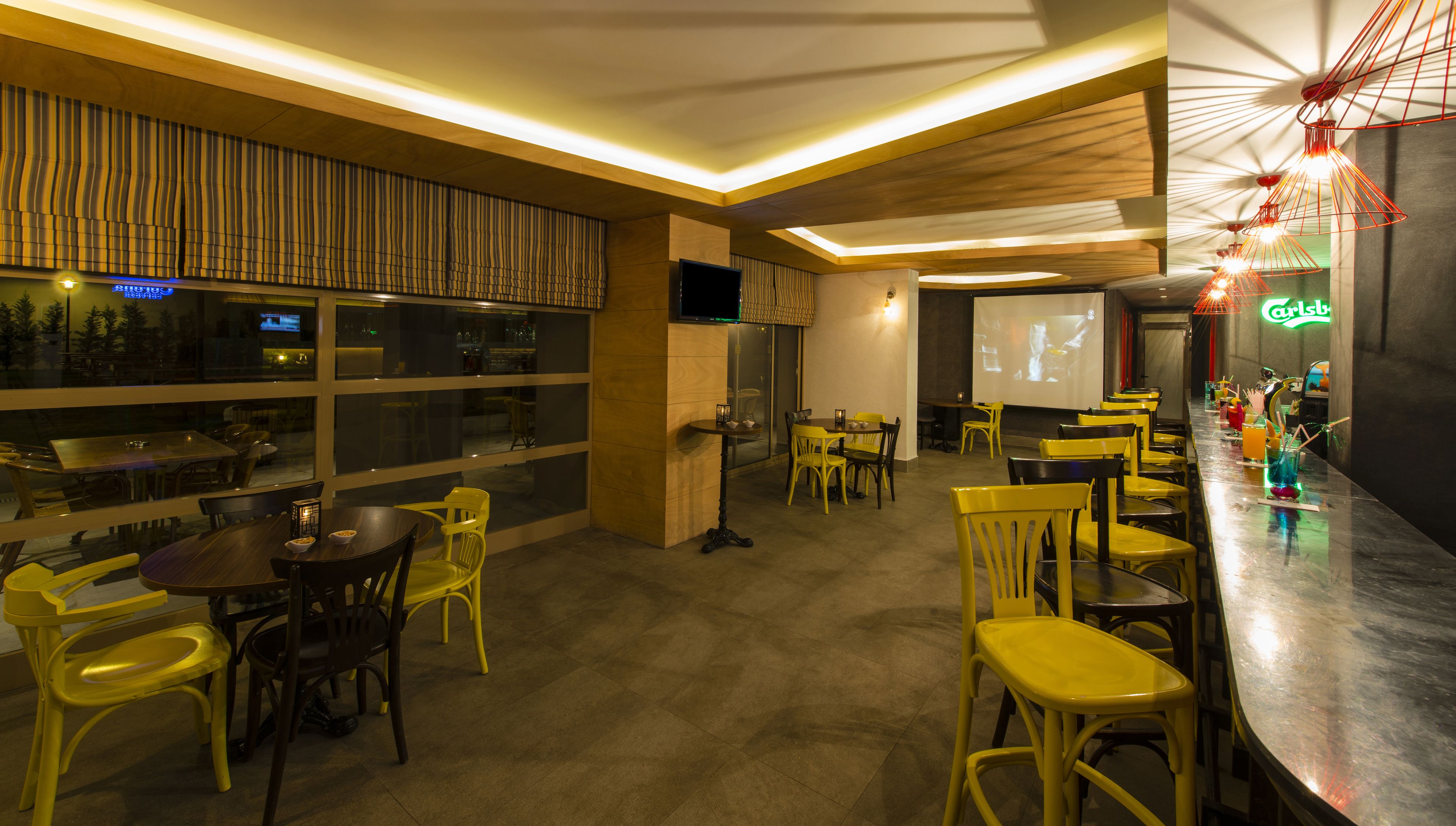 A restaurant with a bar area, tables, chairs, and a projection screen.