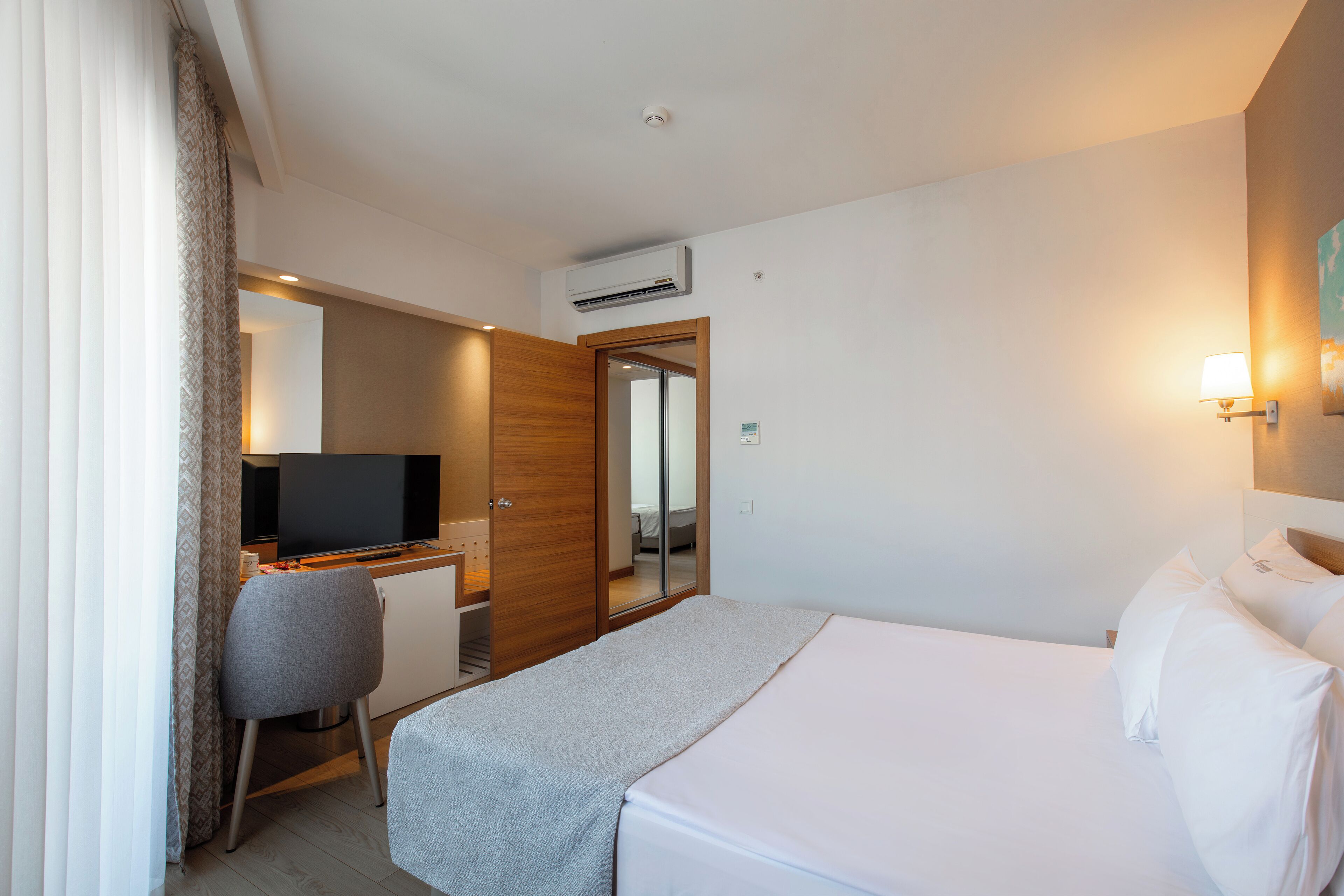 A hotel room with a bed, a desk, a television, and an air conditioning unit.