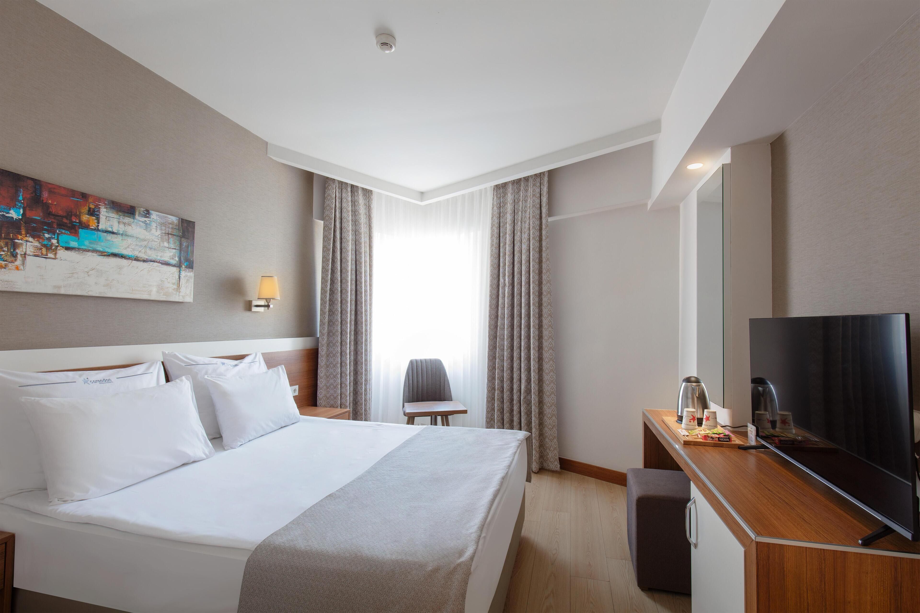 A hotel room with a large bed, a desk with a flat-screen TV, a lamp, and a chair.