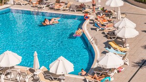 A large outdoor swimming pool with multiple sun loungers and umbrellas, surrounded by palm trees and a grassy area. - Corendon Grand Park Lara - Ultra All Inclusive (Antalya)