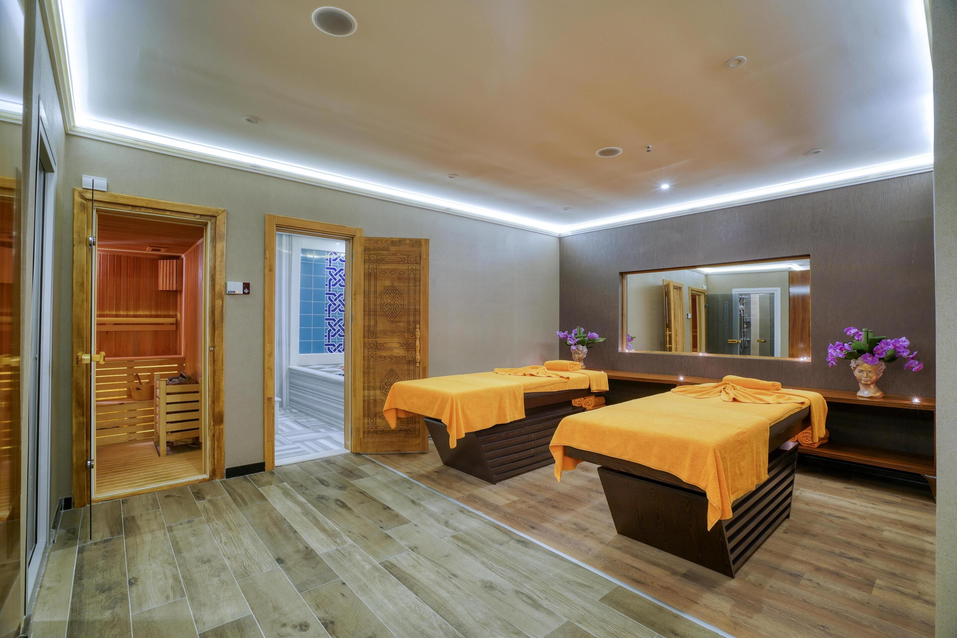 A spa room with two massage tables, a wooden cabinet, and a mirror on the wall.