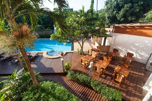 Une terrasse en bois avec une piscine, du mobilier d’extérieur et une végétation luxuriante.