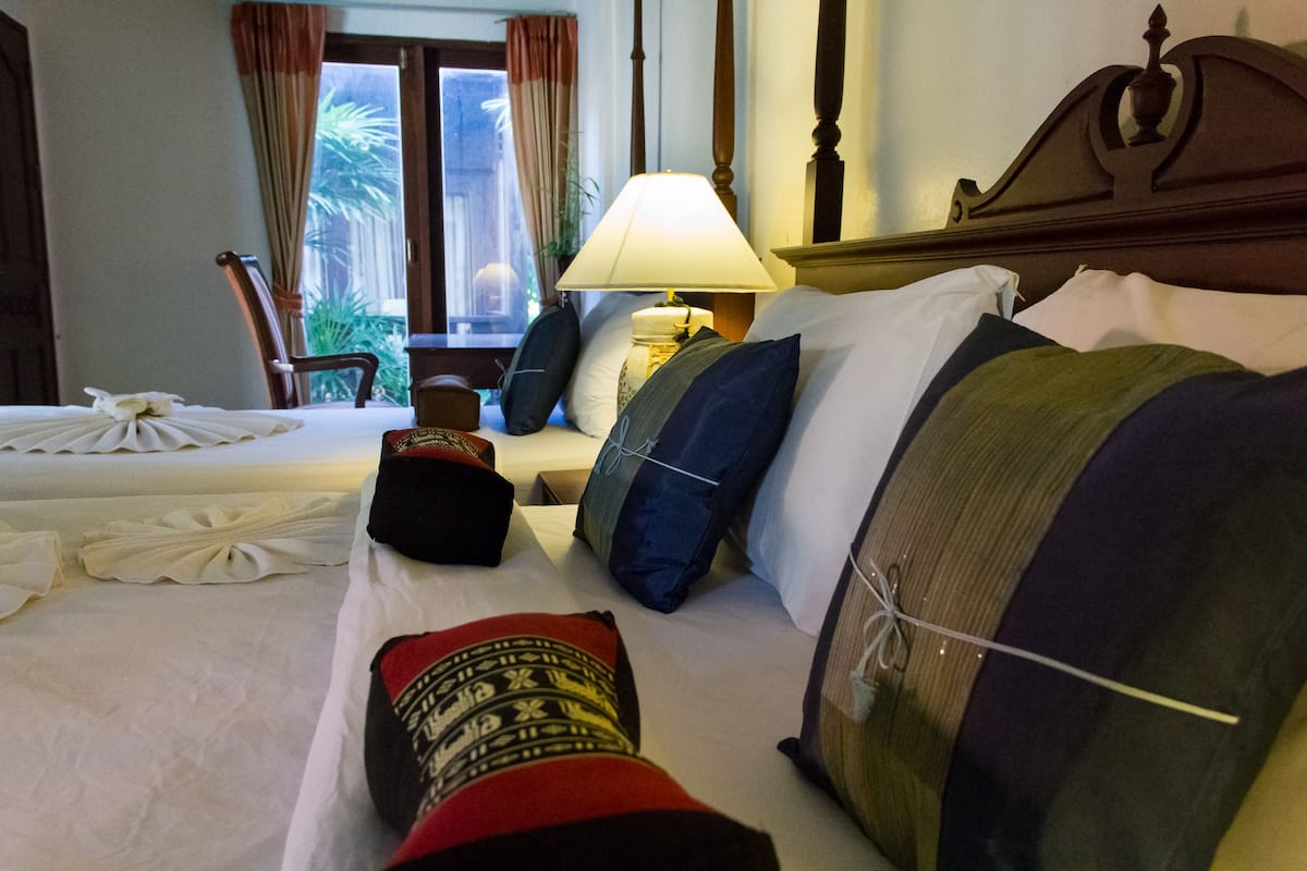 A hotel room with a neatly made bed, a bedside lamp, and a view of the outdoors through a window.