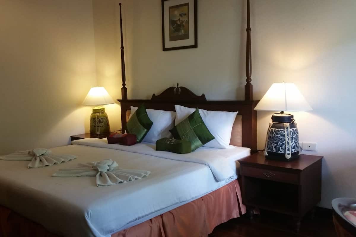 A hotel room with a neatly made bed, two bedside tables, a nightstand, and a lamp on each side of the bed.