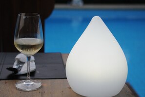 A glass of white wine and a white, teardrop-shaped light fixture on a wooden table by a pool. - Phangan Paragon Resort & Spa (Ko Pha-ngan)