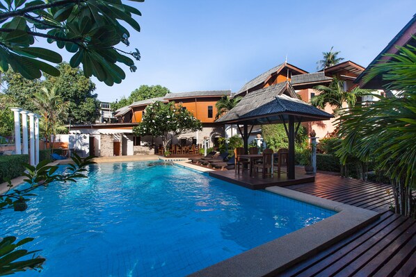 A swimming pool with lounge chairs and a gazebo, surrounded by tropical plants and buildings with traditional architecture. - Phangan Paragon Resort & Spa (Ko Pha-ngan)