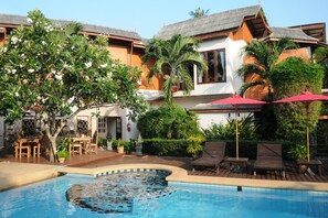 A pool area with lounge chairs and a dining table, surrounded by lush greenery and a building with a tiled roof. - Phangan Paragon Resort & Spa (Ko Pha-ngan)