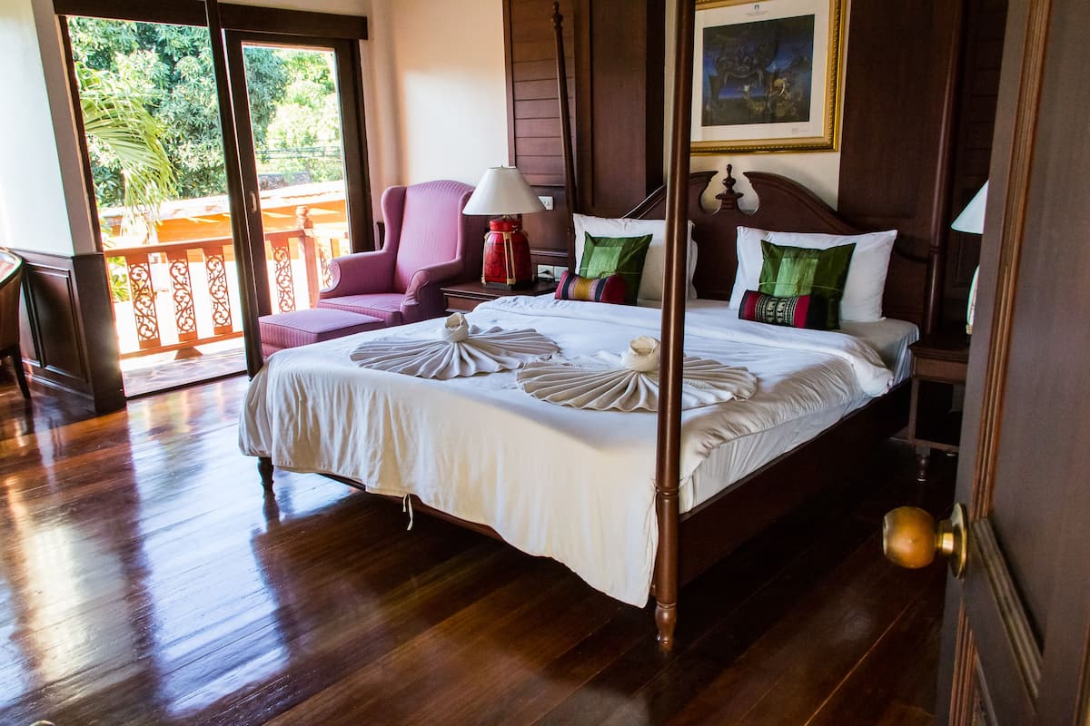 A well-appointed bedroom with a four-poster bed, a chair, and a balcony view.