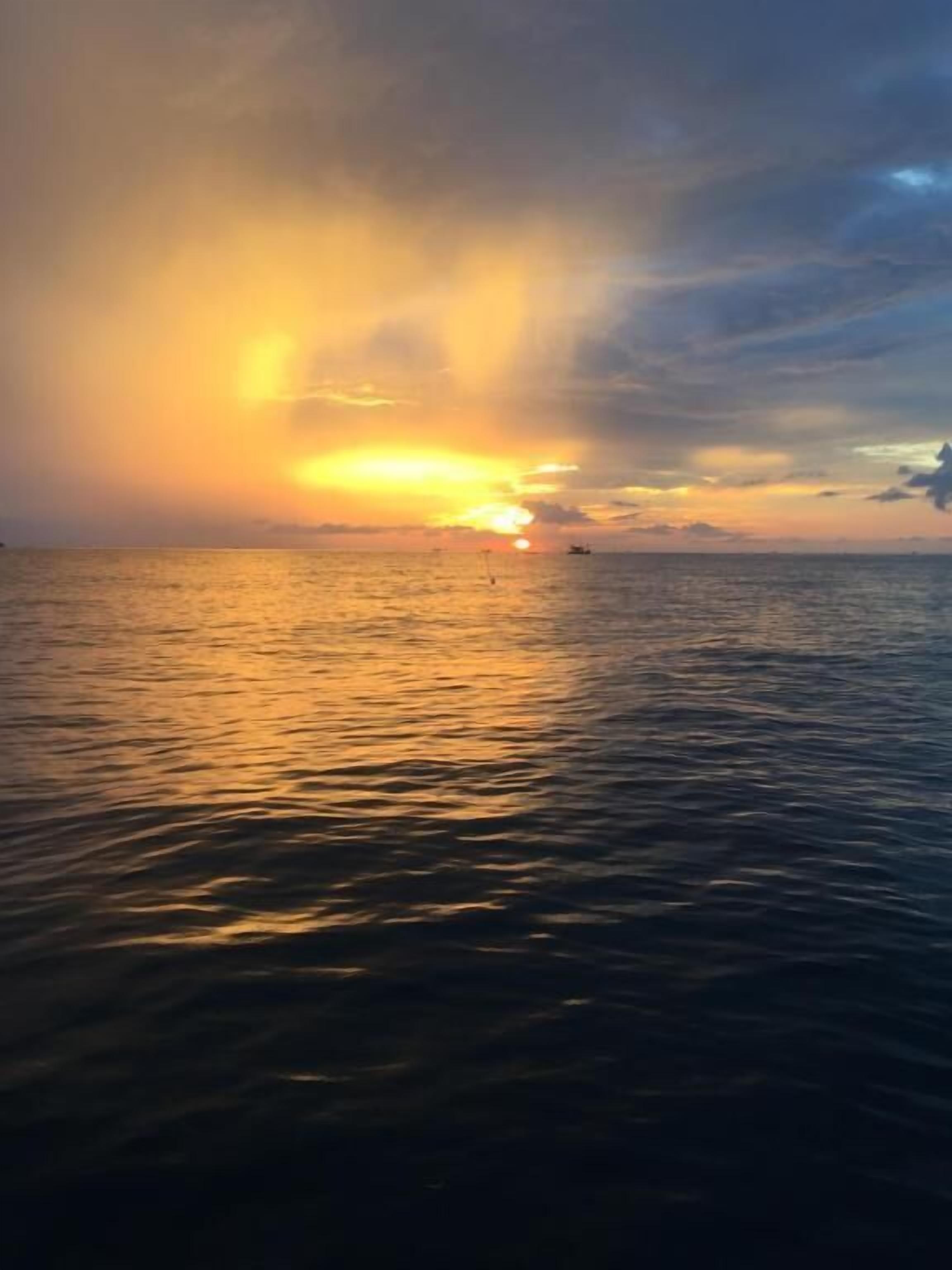 Un atardecer sobre un mar tranquilo con un barco a lo lejos.