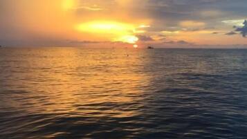 Un atardecer sobre un mar tranquilo con un barco a lo lejos.