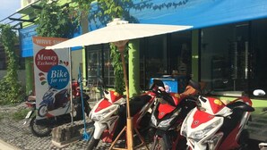 A row of red and white motorcycles parked outside a building with a blue awning. - Maehaad Guesthouse (Ko Pha-ngan)