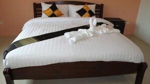 A neatly made bed with white linens, a black and yellow pillow, and a folded towel on the bed. - Maehaad Guesthouse (Ko Pha-ngan)