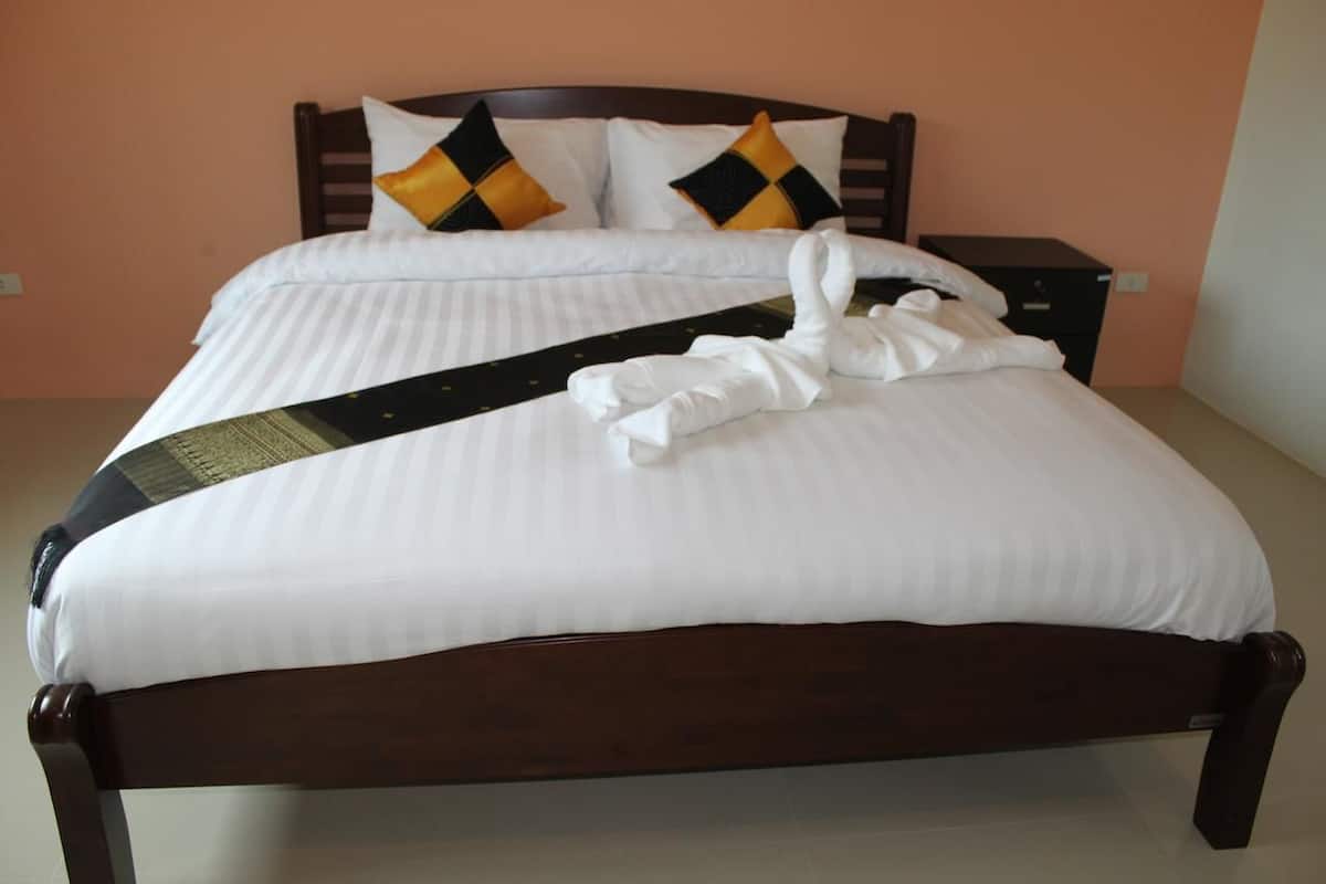 Een net opgemaakt bed met witte lakens, een zwart-geel kussen en een opgevouwen handdoek op het bed.