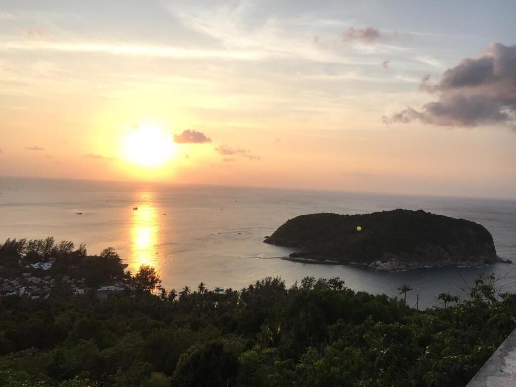 Vista de um pôr do sol à beira-mar com uma pequena ilha ao longe.