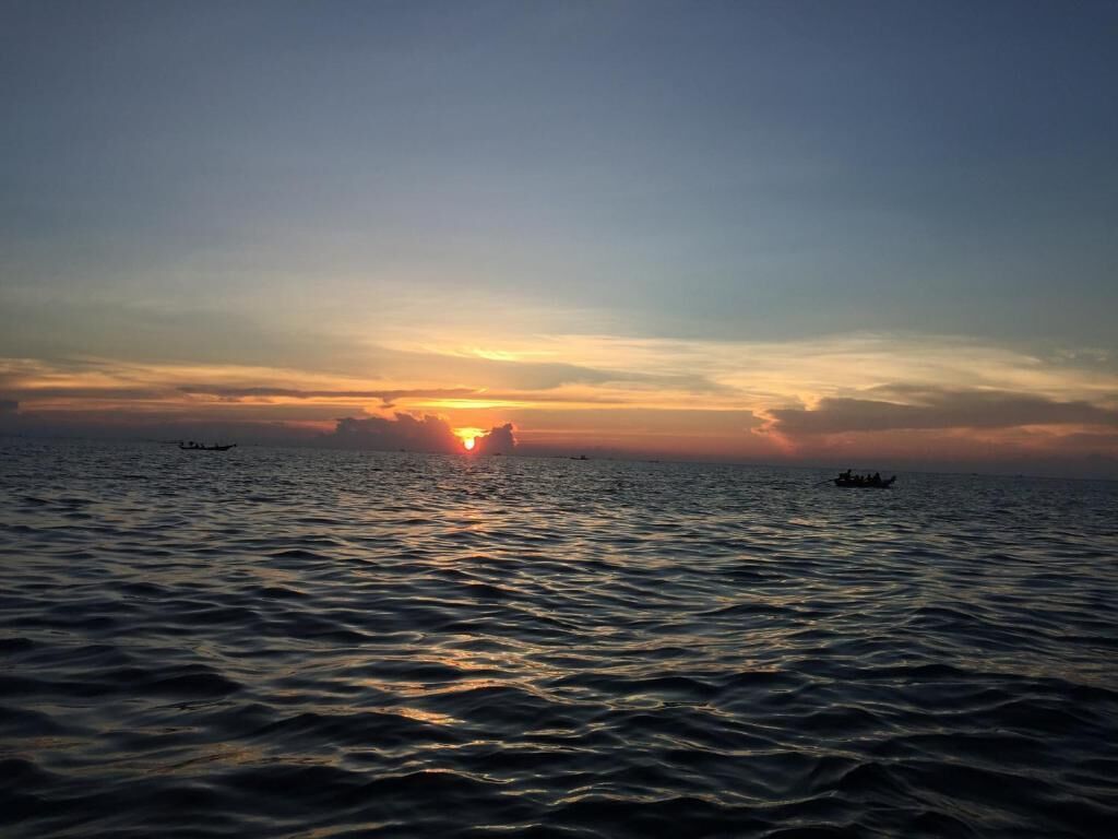 Un atardecer sobre un mar tranquilo con barcos a lo lejos.