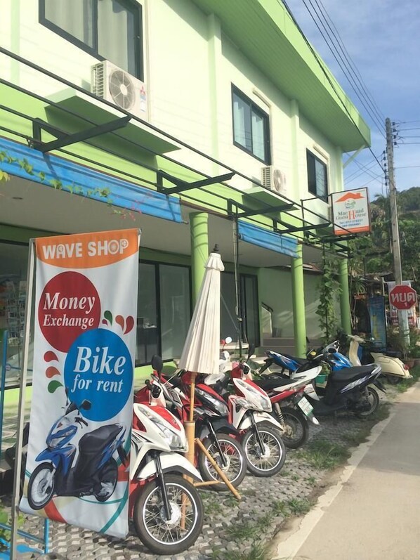A building with a green facade, a 'Wave Shop' sign, and a 'Money Exchange' sign. There are several motorcycles parked in front. - Maehaad Guesthouse (Ko Pha-ngan)