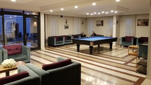 Une pièce spacieuse avec une table de billard, plusieurs canapés et un sol à carreaux.