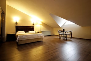 Un dormitorio con cama, mesitas de noche, un escritorio con sillas y un tragaluz.