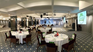 Une salle de conférence équipée de tables rondes, de chaises et d’un écran de présentation.