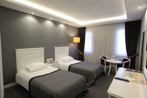 Habitación de hotel con dos camas, un escritorio, una silla, una lámpara y una ventana con cortinas.