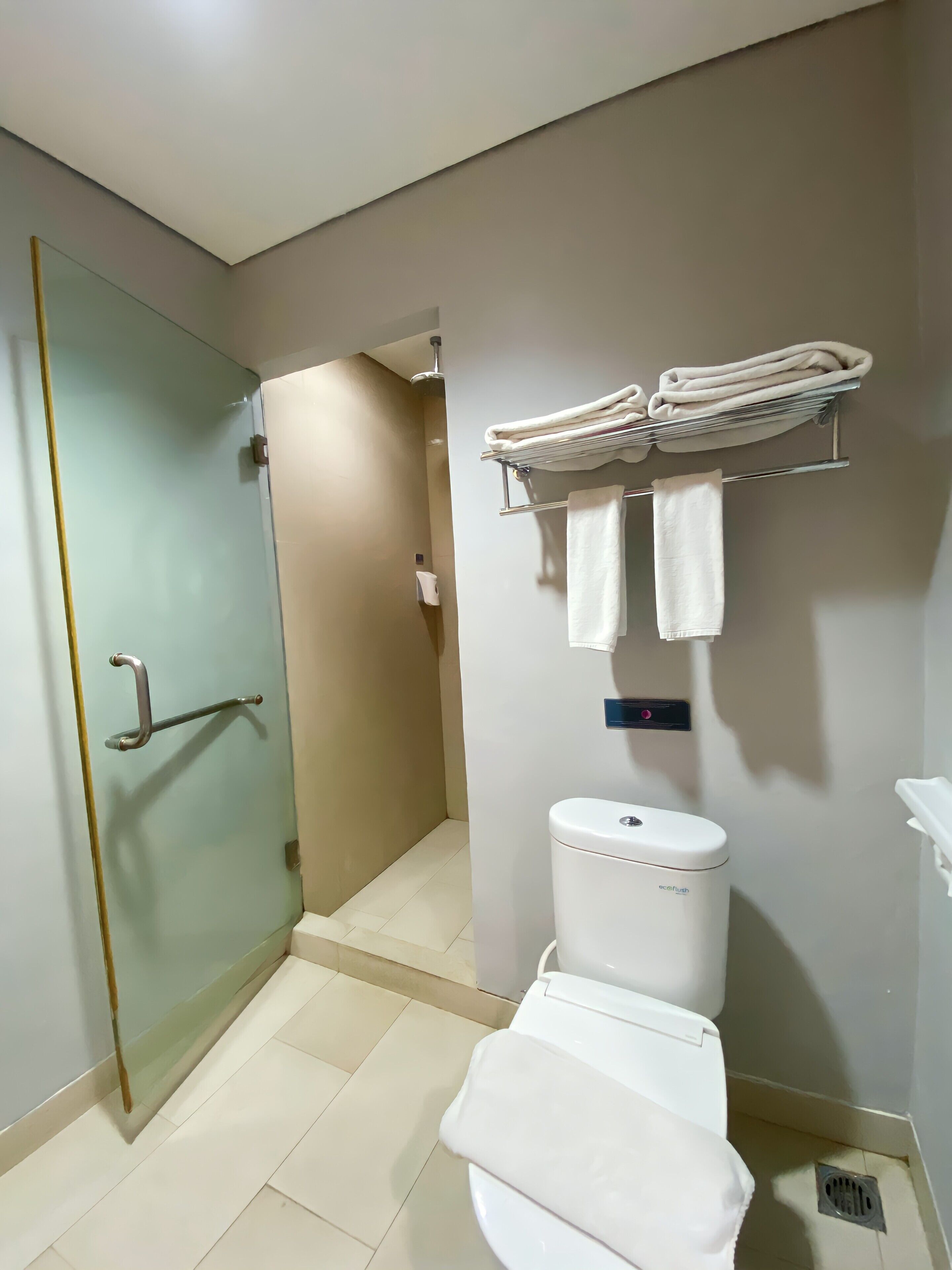 Un baño con mampara de vidrio, inodoro y toallero con toallas dobladas.