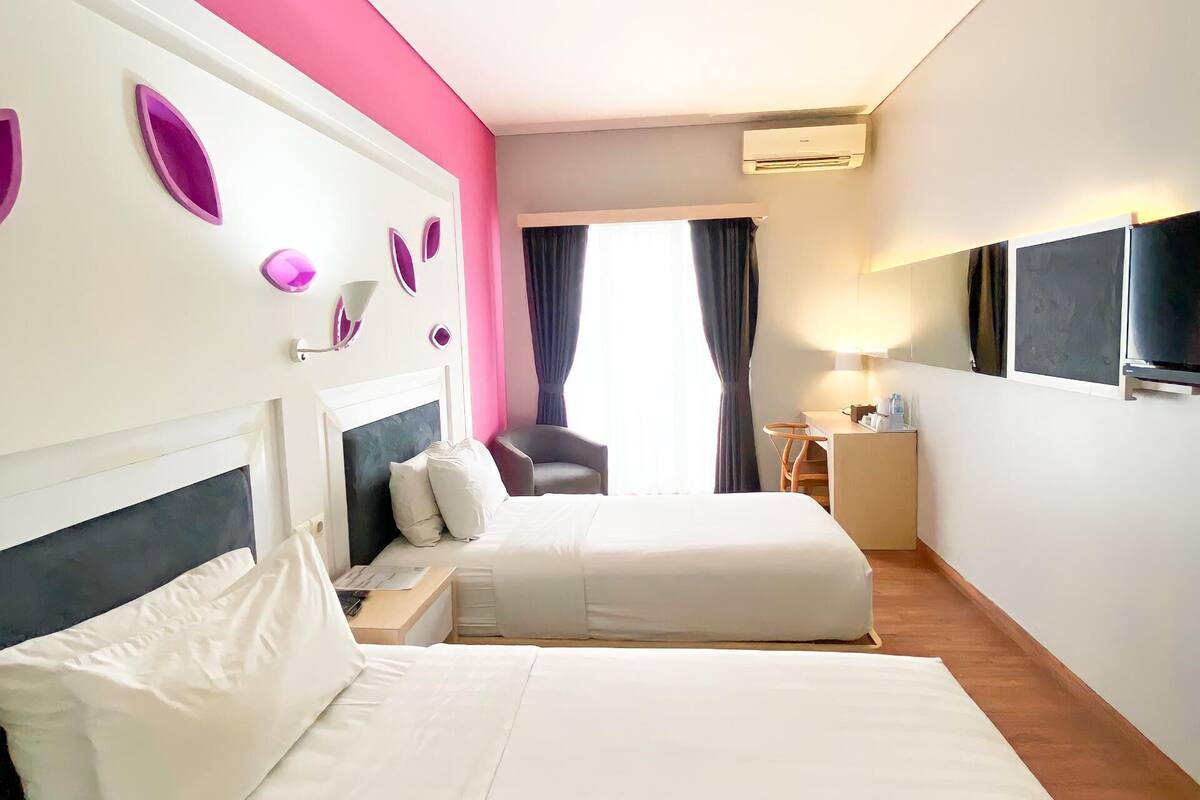 Ein Hotelzimmer mit zwei Betten, einem Fernseher, einem Schreibtisch und einem fenster mit Vorhängen.