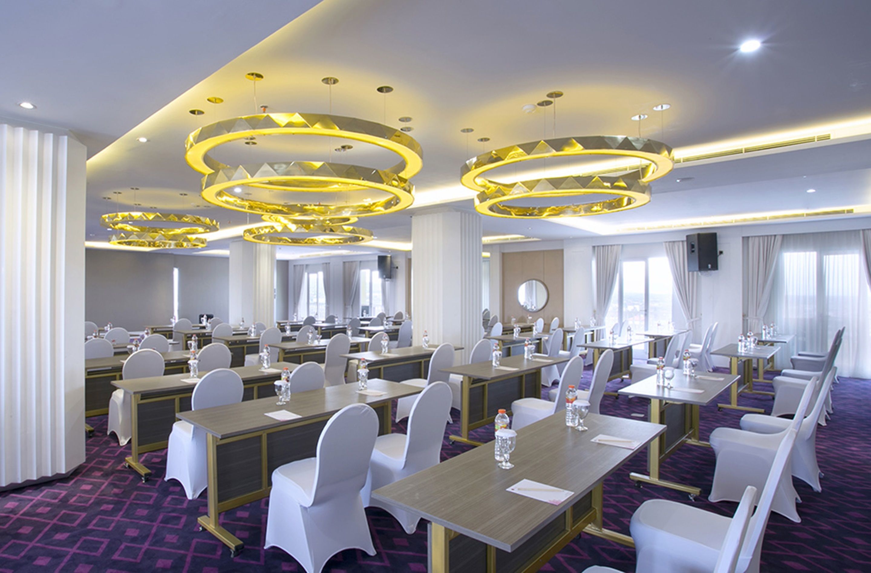 A conference room with multiple tables, chairs, and modern chandeliers.