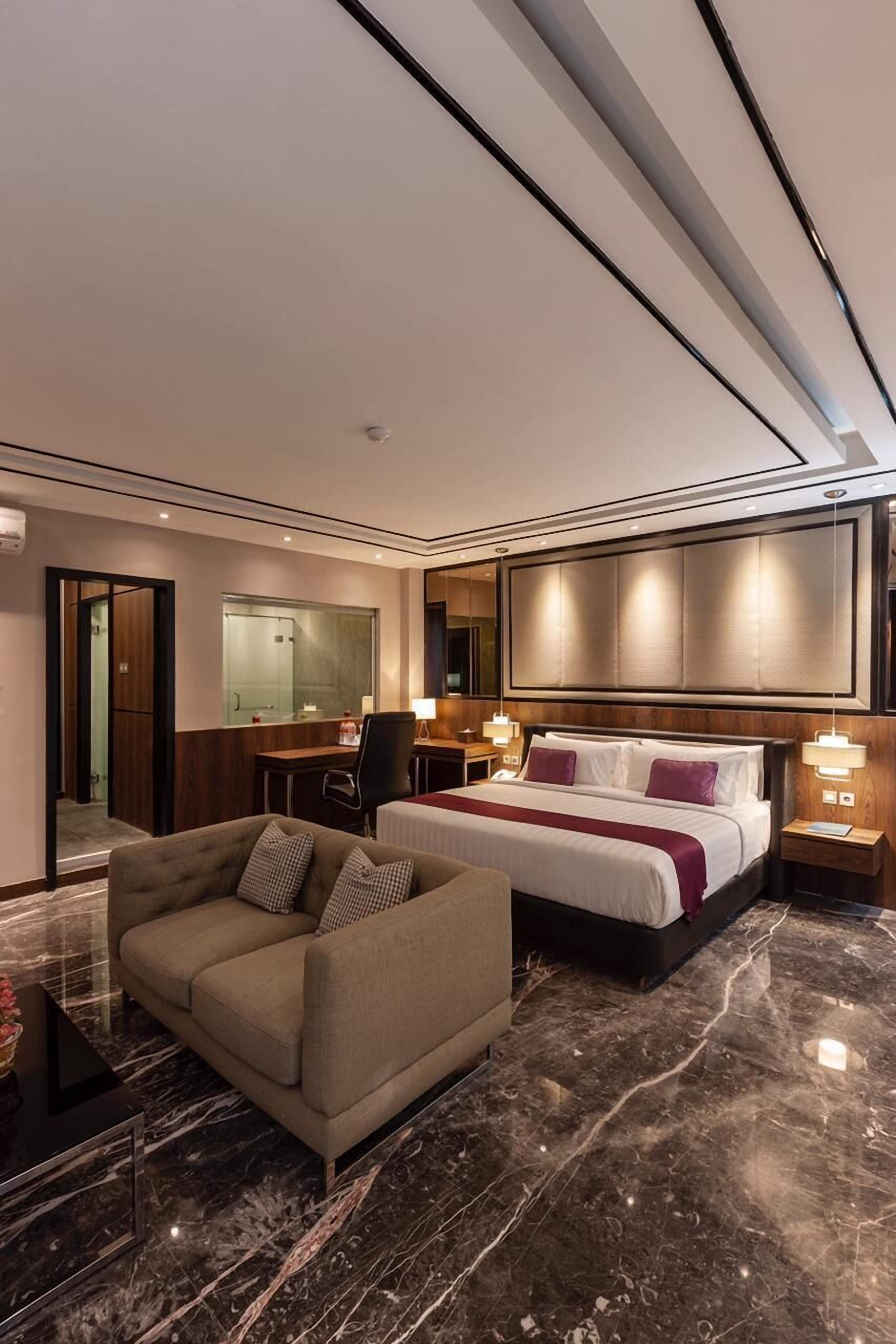 A modern hotel room with a large bed, a sofa, a desk, and a mirror.