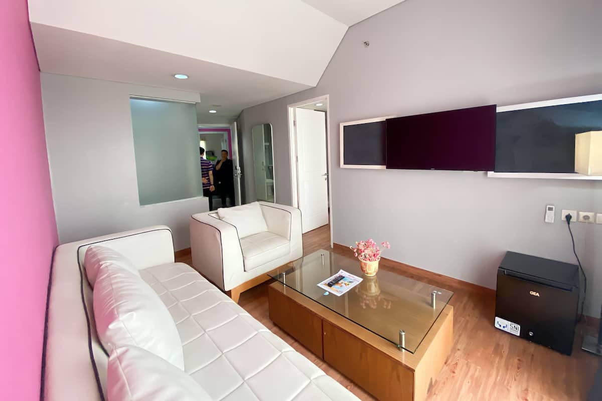 Ein modernes Hotelzimmer mit einem Glastisch, einer Couch, einem an der Wand befestigten Fernseher und einem kleinen, schwarzen Safe.