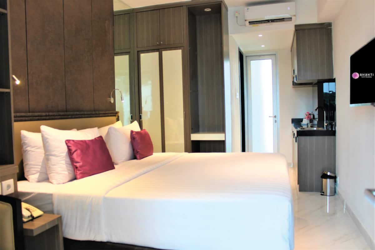 Ein Hotelzimmer mit einem großen Bett, einem Nachttisch mit Telefon, einer kleinen Mülltonne und einer Küchenzeile mit Fernseher.