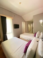A hotel room with two beds, a television, a mirror, and a light fixture.