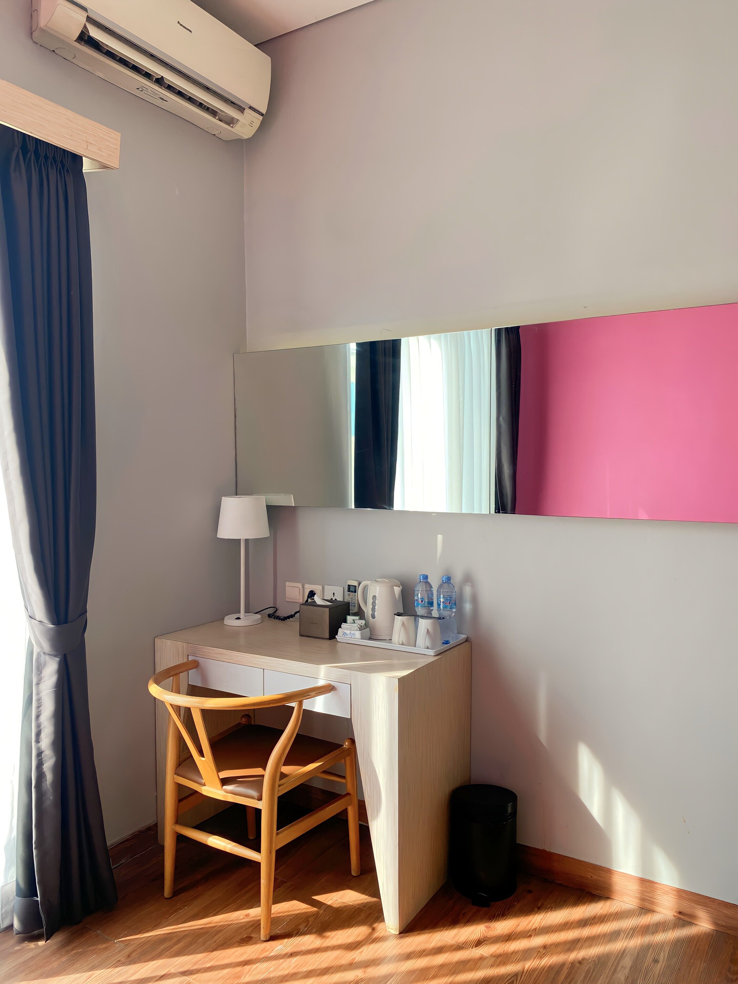 Une chambre d’hôtel équipée d’un bureau en bois, d’une chaise, d’un miroir, d’une lampe, d’une machine à café et d’un distributeur d’eau.