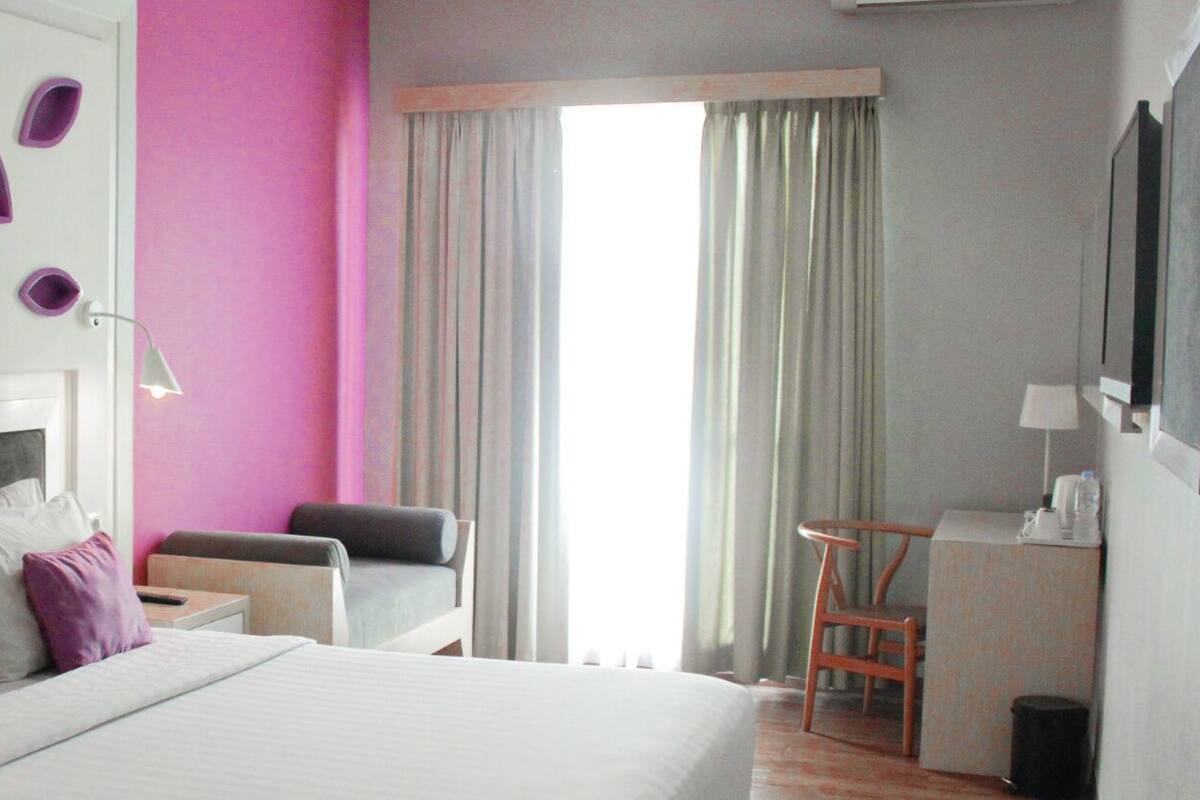 Ein Hotelzimmer mit einem großen Bett, einem Schreibtisch, einem Stuhl und einem Fenster mit Vorhängen.