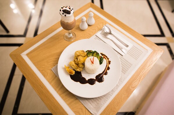 A dining table with a plate of food, a glass of dessert, and salt and pepper shakers.