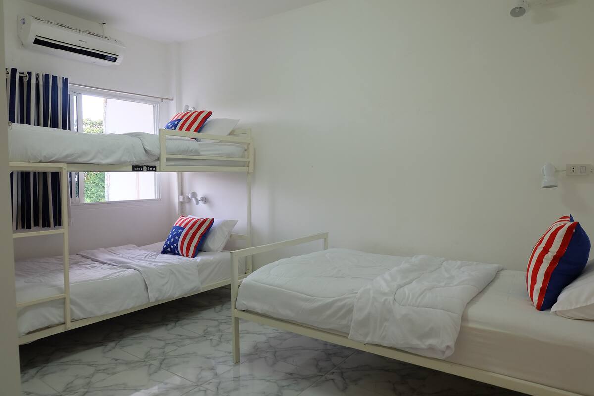 A dormitory room with bunk beds, a window, and an air conditioning unit.