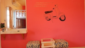 Une pièce avec un mur rouge, un miroir, un autocollant représentant un scooter et deux poufs assortis.