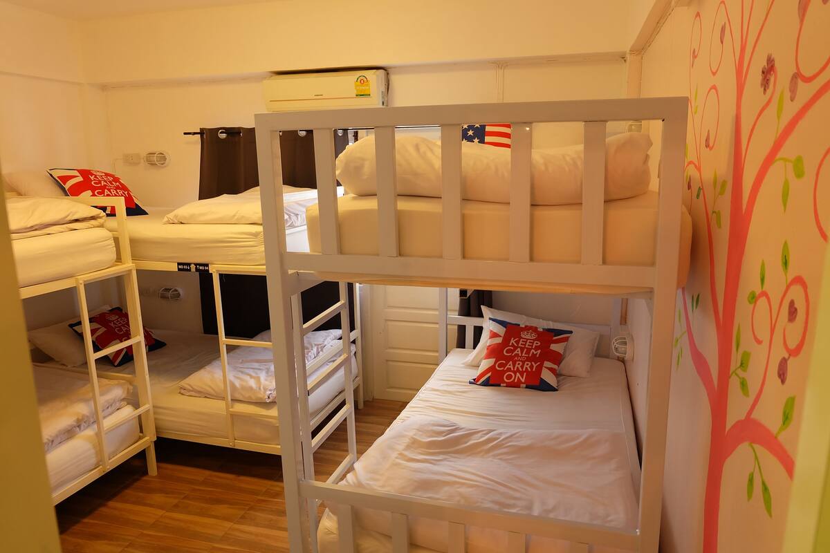 A dormitory room with bunk beds, a bed with a pillow that says "Keep Calm and Carry On," and a wall with a tree design.