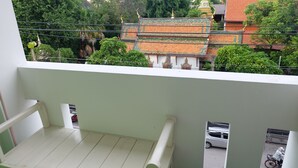 Un balcon donnant sur un temple dont le toit est vert et orange, entouré d’arbres.