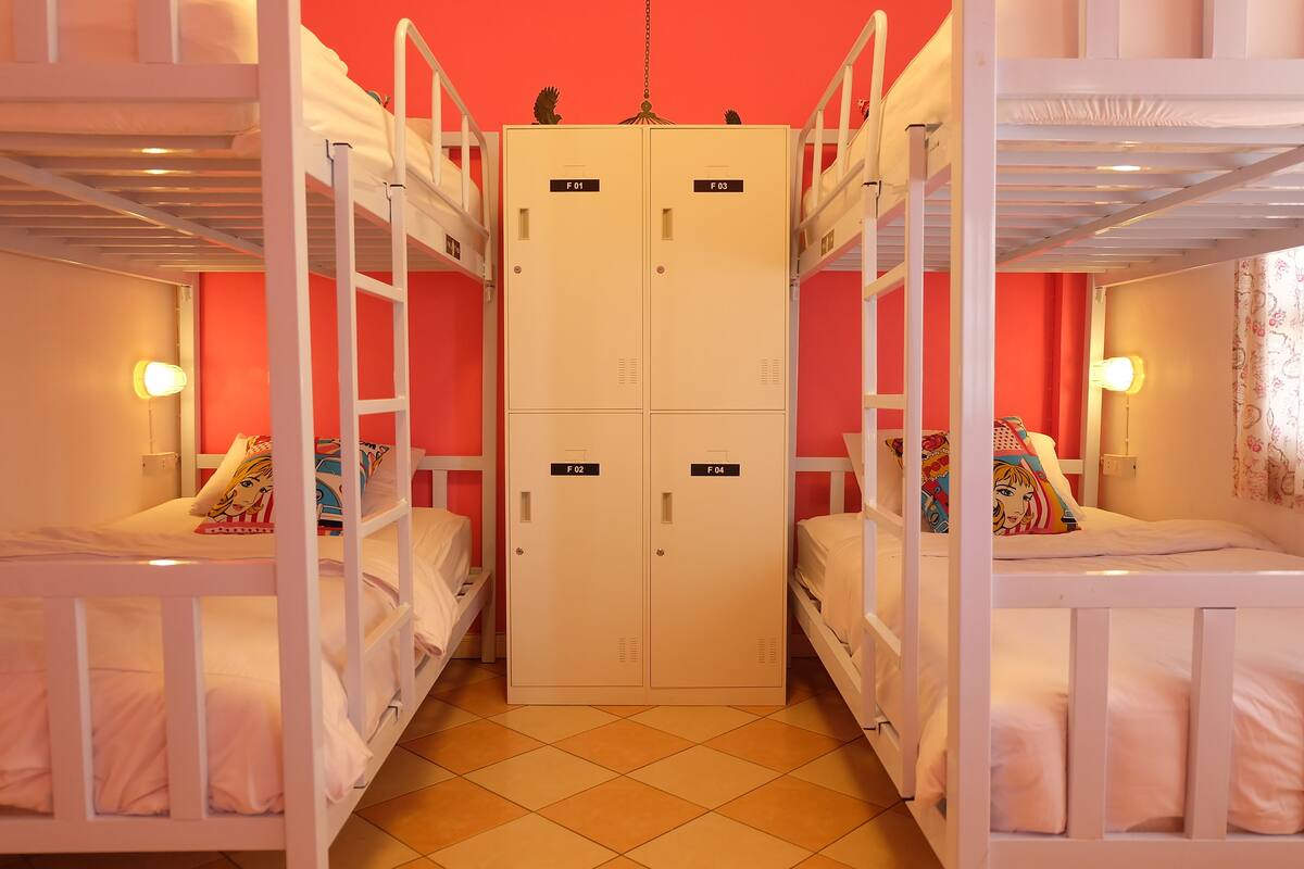 A dormitory room with bunk beds, a central wardrobe, and a tiled floor.