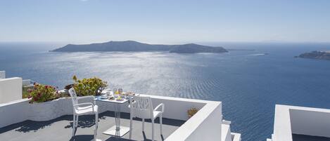 A terrace with white furniture overlooking a clear blue sea and distant islands.