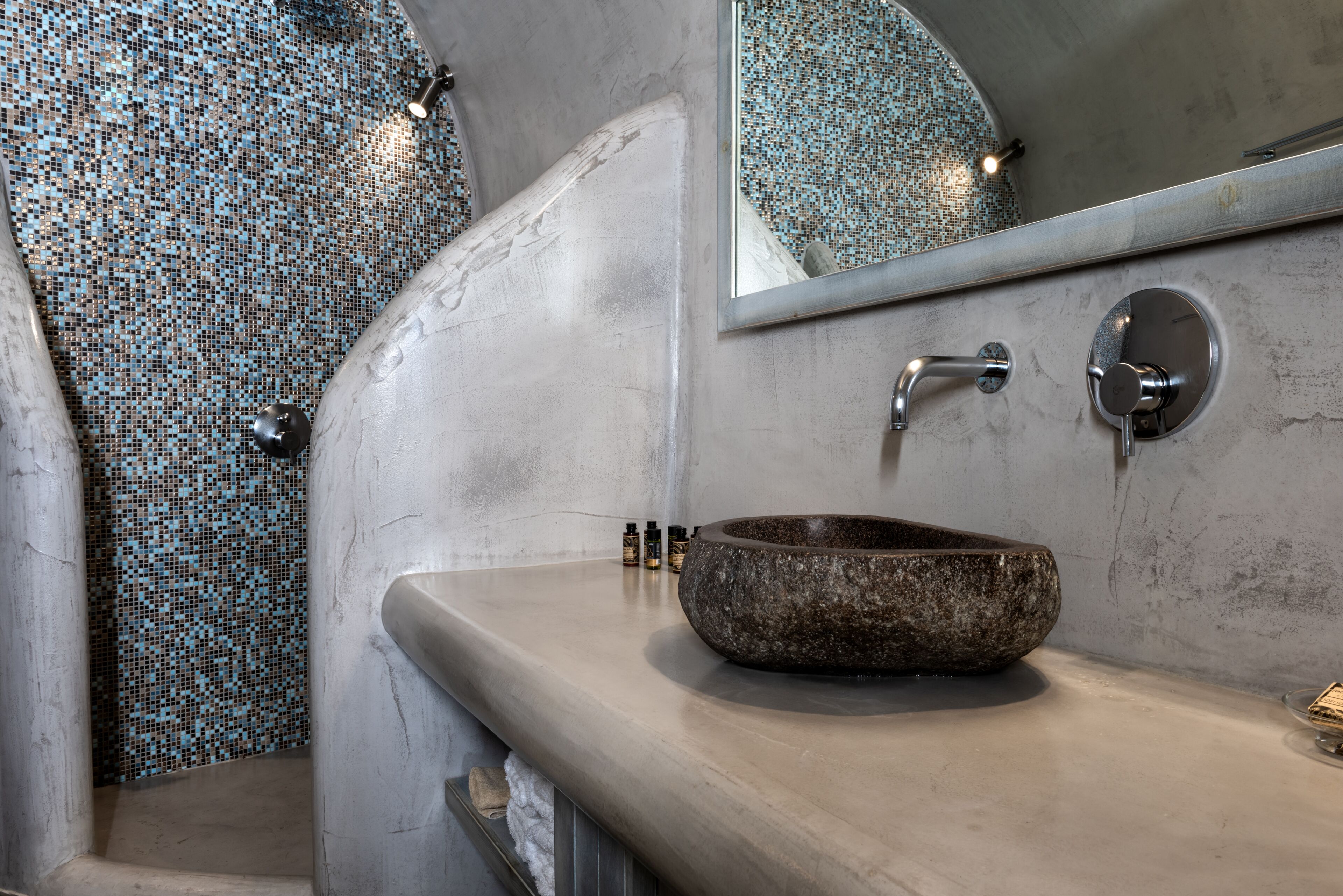 A modern bathroom with a mosaic tile wall, a large basin, and a mirror.