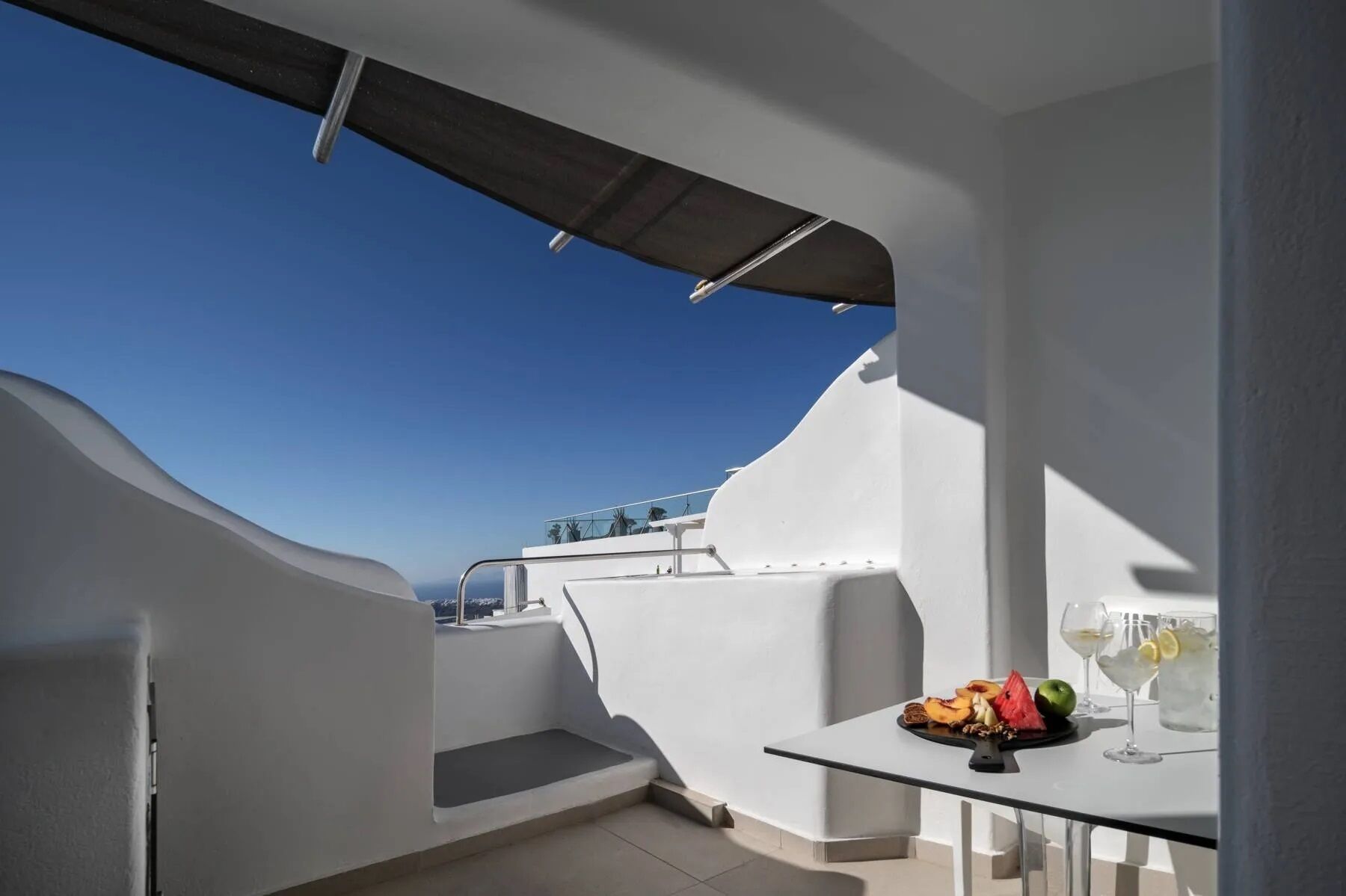Ein moderner Balkon mit freiem Blick auf das Meer, ein Tisch mit Früchten und Getränken, und ein weißes architektonisches Design.