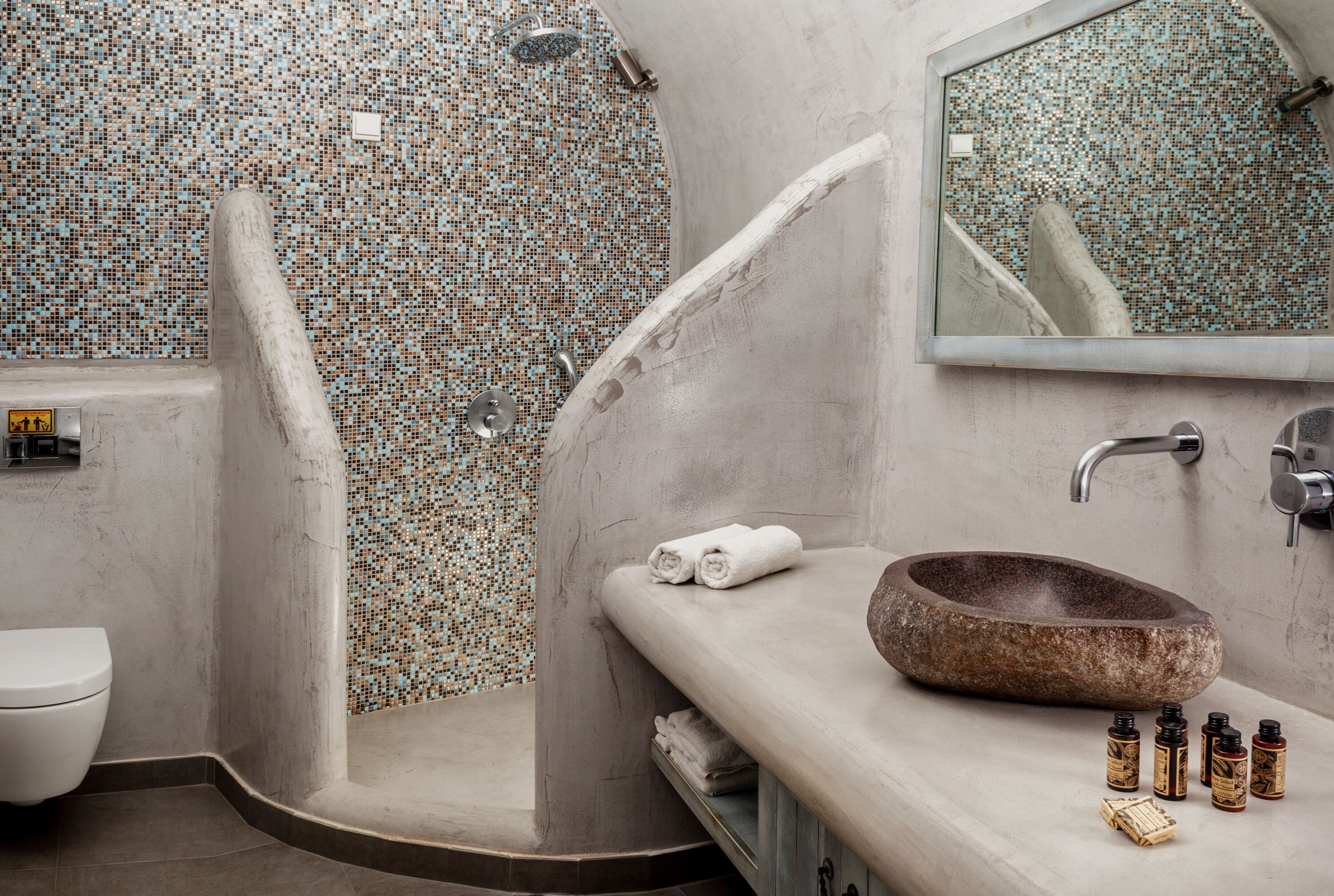Un baño con pared de ducha de mosaico, lavabo de piedra y espejo.