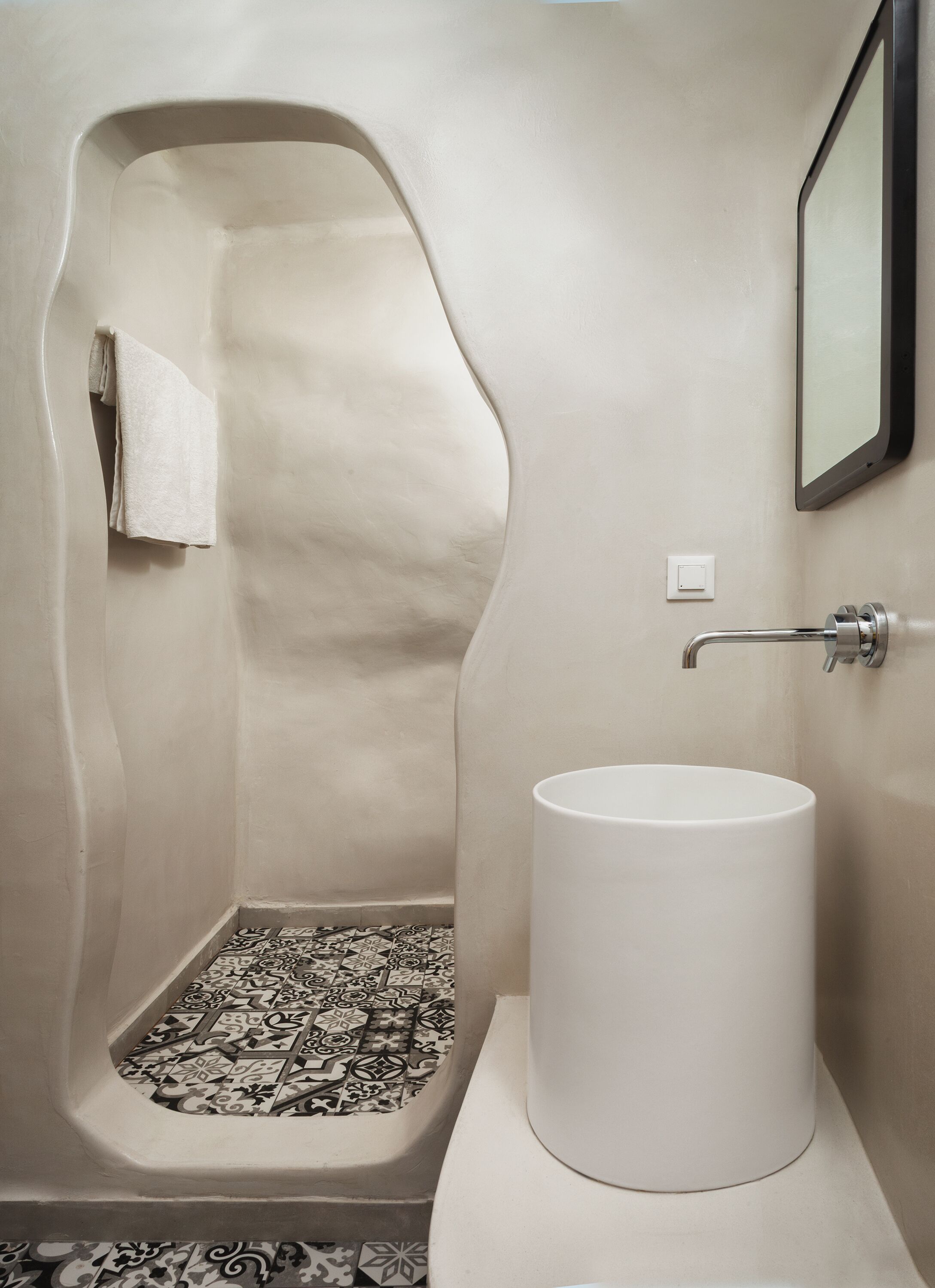 Un baño con un diseño de ducha curvo único, un lavabo blanco y baldosas de suelo estampadas.