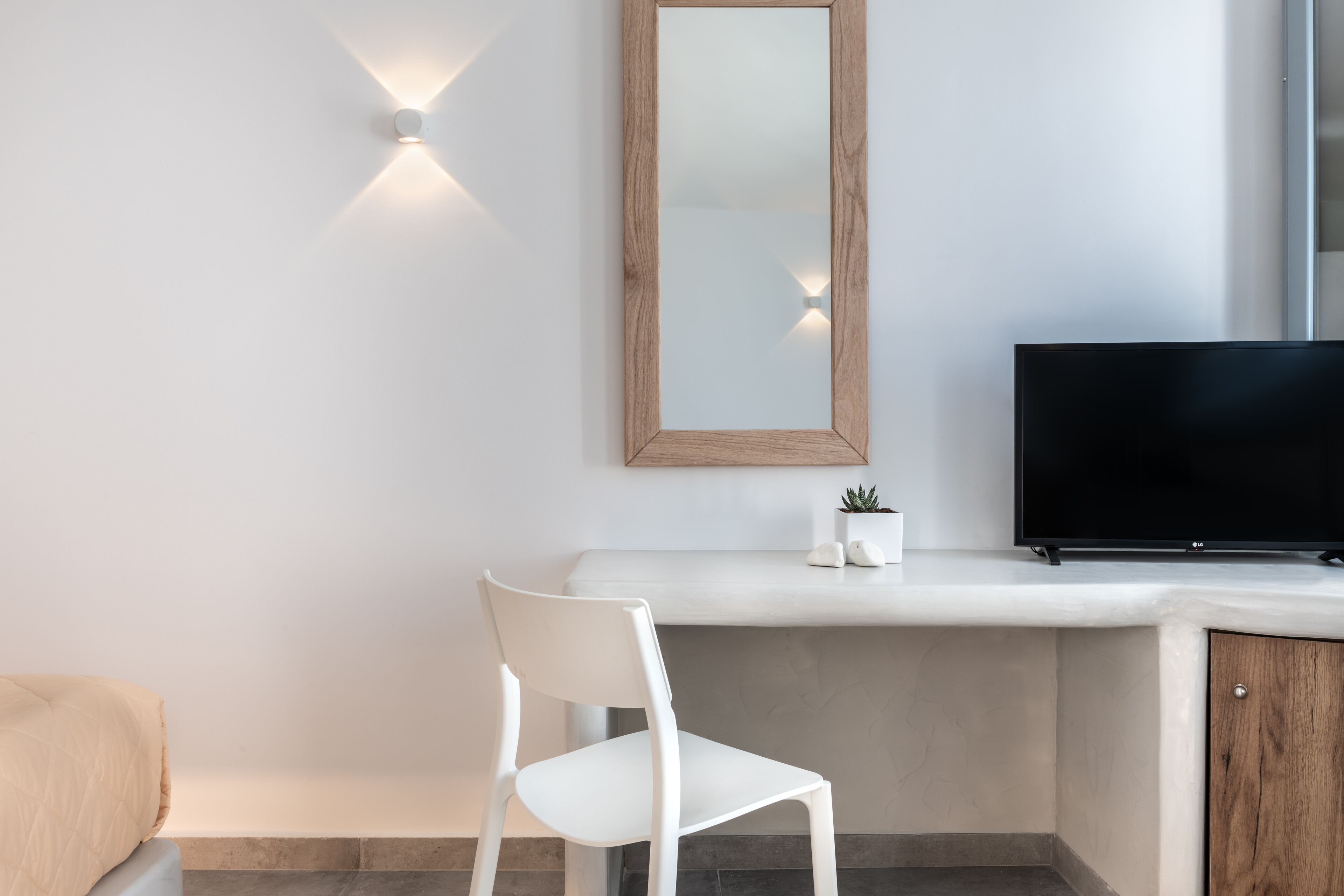 A modern room with a white desk, a flat-screen TV, a white chair, and a wooden-framed mirror.