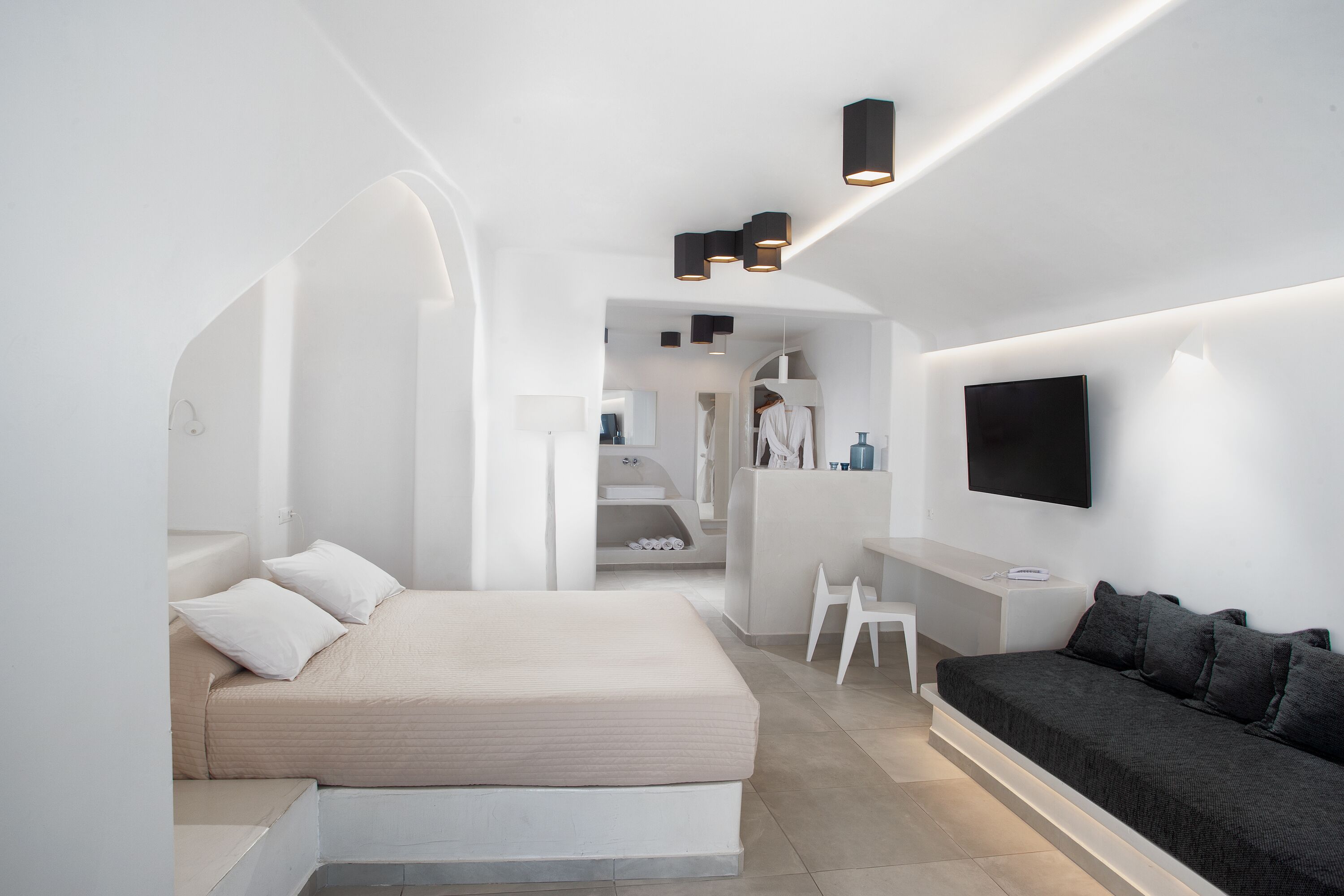 Une chambre à coucher moderne et minimaliste, comprenant un lit, un canapé, une télévision et un bureau.