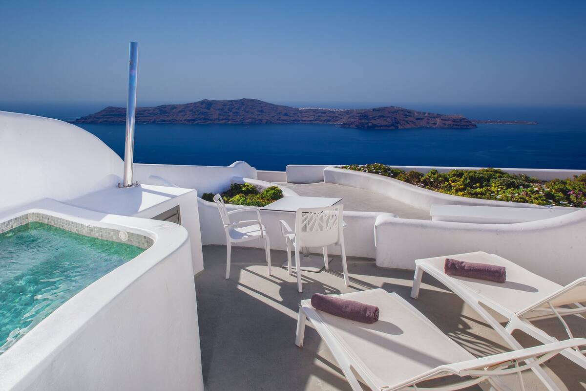 Eine Dachterrasse mit Pool, weißen Liegestühlen und Blick auf das Meer und die Inseln.